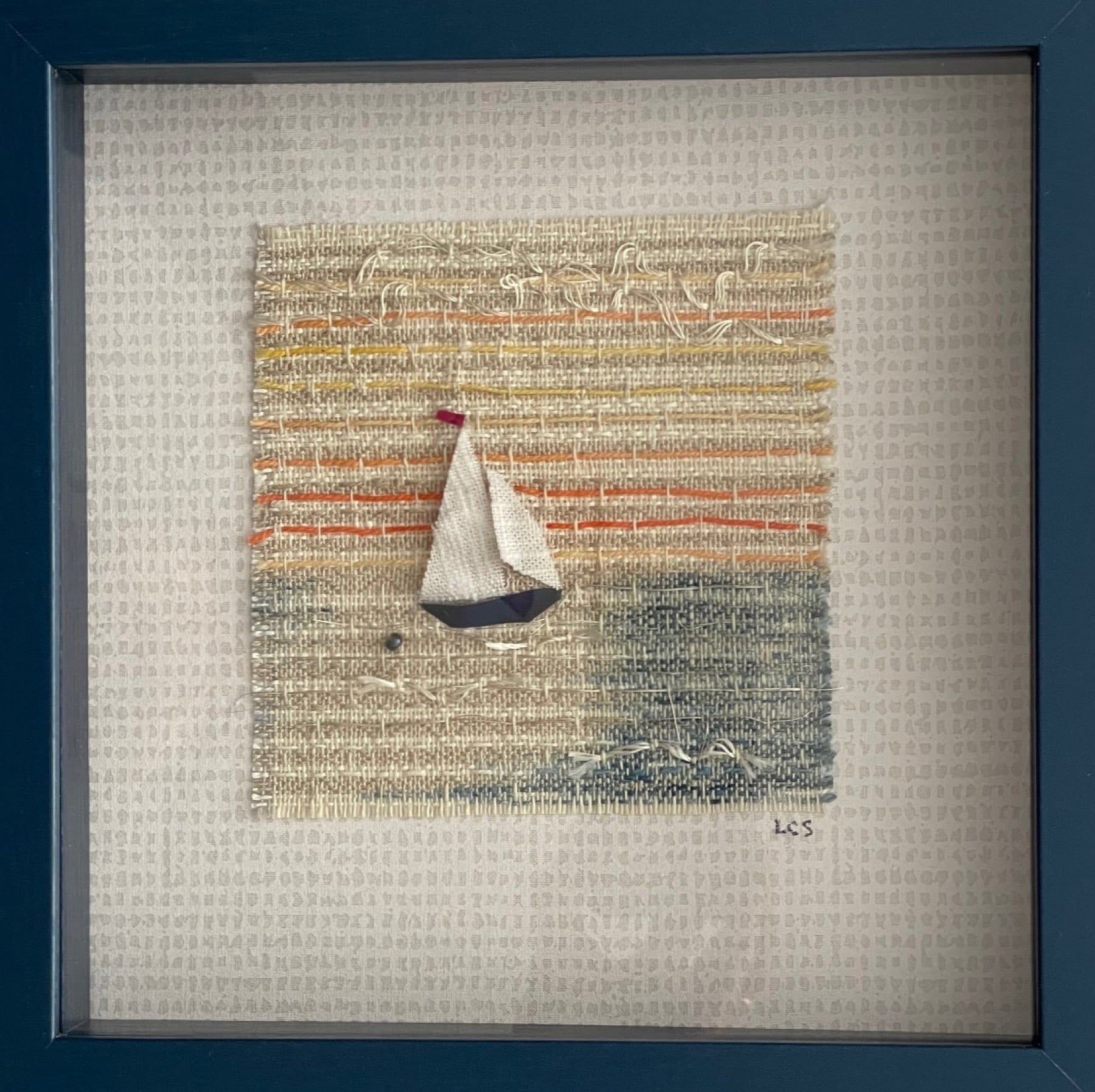 A small framed weaving of a sailboat on a striped sea